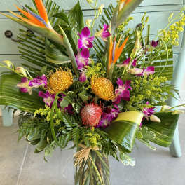 Tropical bouquet with orange bird-of-paradise and purple orchids in a glass vase