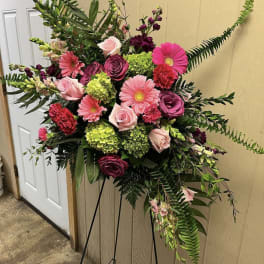 Standing floral spray with pink and burgundy blooms on a black easel