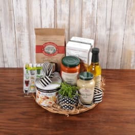Gourmet food gift basket with assorted jars, boxes, and a small potted plant on a wicker tray.