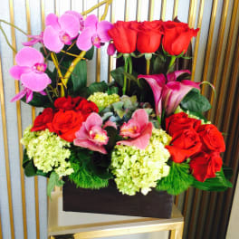 Arrangement of red roses, pink orchids, and calla lilies in a dark box