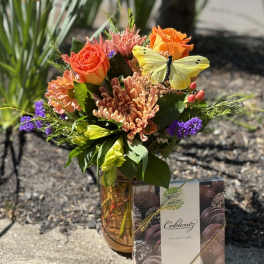 Mixed bouquet in a vase with a box of chocolates beside it