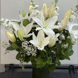 White lilies and buds arranged in a green vase with baby's breath