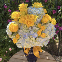 Yellow roses and blue hydrangeas in a dark vase with a yellow ribbon