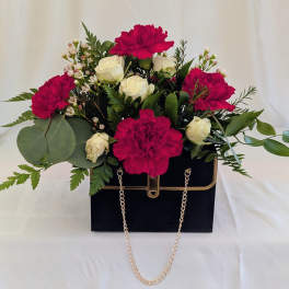Pink carnations and white roses in a black handbag-style box