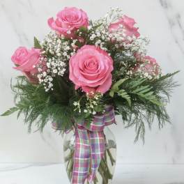 Pink roses in a glass vase with baby's breath and a plaid ribbon
