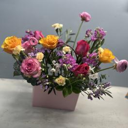Mixed bouquet of pink, yellow, and purple flowers in a pink box