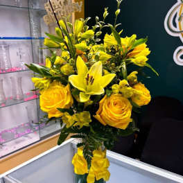 Yellow roses and lilies in a glass vase with a yellow ribbon