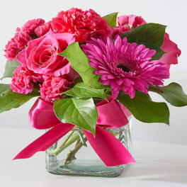 Pink roses, carnations, and a gerbera daisy in a glass vase with a pink ribbon