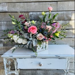 Mixed pink and white floral arrangement in a square container on a white table
