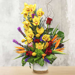 Tall tropical bouquet with yellow orchids, red roses, and orange bird-of-paradise in a glass vase
