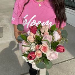 Handheld bouquet of pink roses and red tulips with greenery