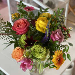 Mixed bouquet of colorful roses, gerbera daisies, and other blooms in a glass vase