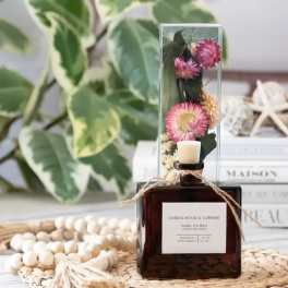 A reed diffuser bottle with dried pink flowers in a clear tube