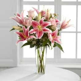 Pink lilies and roses arranged in a tall clear vase