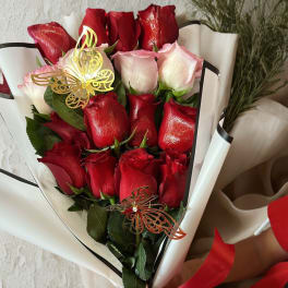 Bouquet of red and pale pink roses wrapped in white paper with a red bow