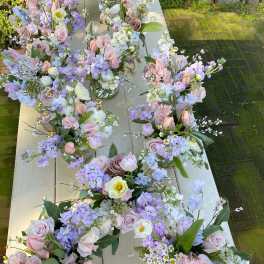 Pastel floral bouquets arranged in small glass vases on a long table outdoors.