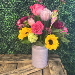 Mixed bouquet of pink roses, tulips, and yellow sunflowers in a pale vase