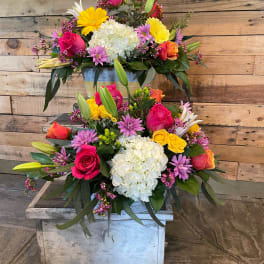 Two colorful floral arrangements in metal containers with roses, hydrangeas, lilies, and daisies