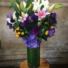 Mixed bouquet of lilies, roses, and hydrangeas in a tall green vase