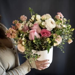 Handheld bouquet of pink and white roses in a white container