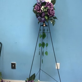 Purple floral arrangement on a tall black stand with hanging greenery