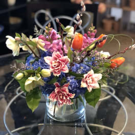 Mixed bouquet in a clear glass vase with blue, pink, orange, and white flowers