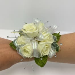 Wrist corsage of ivory roses with iridescent ribbon and crystal bead accents on an arm.