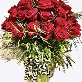 Tall arrangement of red roses with cascading greenery in a green vase with a chevron bow.