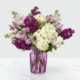 Purple and white mixed flower bouquet in a purple glass vase