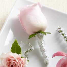 A pale pink rose boutonniere with white ribbon and pearl accents