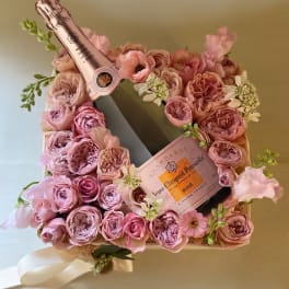 Pink rose arrangement with two champagne bottles in a gift box