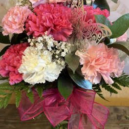 Pink and white carnations with a butterfly decoration in a glass vase