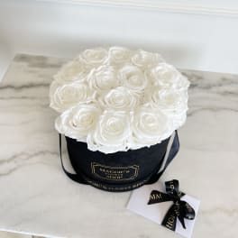 White roses arranged in a black round box with a ribbon and card