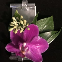 Purple orchid boutonniere with green leaves on a clear clip
