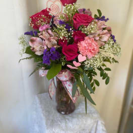 Pink and purple bouquet in a glass vase with heart picks