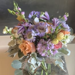 Pastel bouquet of peach, pink, and purple flowers in a glass vase
