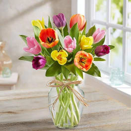 Colorful tulips arranged in a clear glass vase with a raffia bow