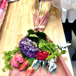 Bouquet of purple hydrangea, pink tulips, and a red rose wrapped in pink paper
