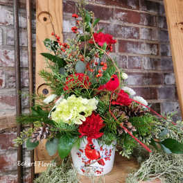 Holiday floral arrangement in a bird-decorated pot with pinecones and red blooms