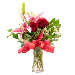 Red roses and pink lilies in a clear glass vase with a red ribbon