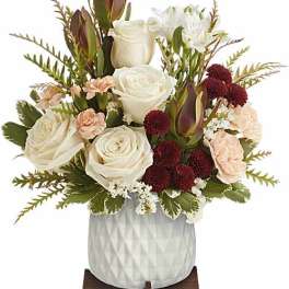White roses, burgundy blooms, and peach flowers in a white vase