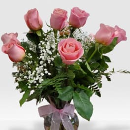 Glass vase of pink roses with white filler flowers and a pink ribbon bow