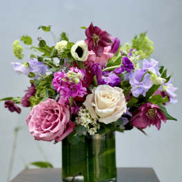 Pink and white roses with purple blooms in a glass vase
