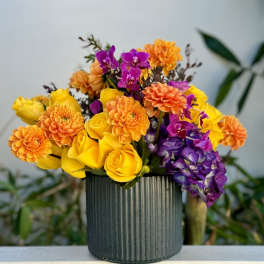 Bouquet of yellow roses, orange dahlias, and purple orchids in a ribbed vase