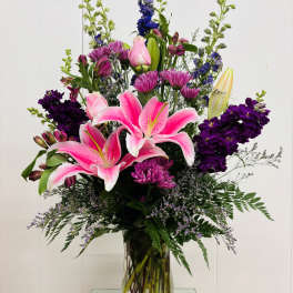 Pink lilies and purple flowers arranged in a clear glass vase