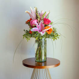 Tall bouquet of pink lilies and orange flowers in a glass vase