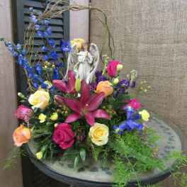 Mixed bouquet with roses, lilies, and an angel figurine in a low vase