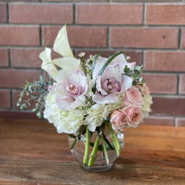 Bouquet of white orchids, pale pink roses, and white hydrangeas in a glass vase