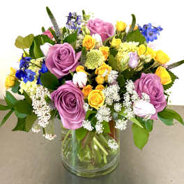 Mixed bouquet of purple, yellow, and blue flowers in a glass vase