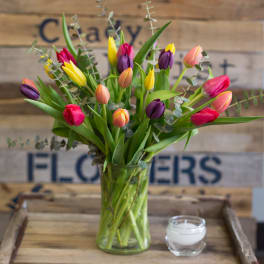 Colorful tulips in a glass vase with a small candle beside it